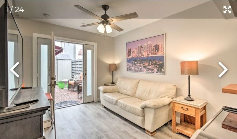 Cozy living room with beige sofa and open door to outdoor patio.