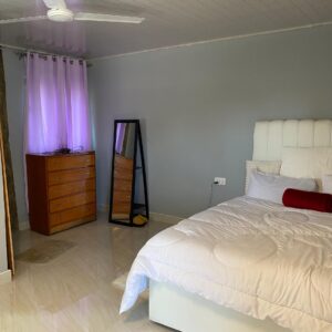 Cozy bedroom with white bedding, wooden dresser, and standing mirror.